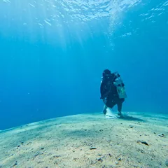 צולל עומד על קרקעית החול במים כחולים, וקרני אור יורדות מלמעלה.